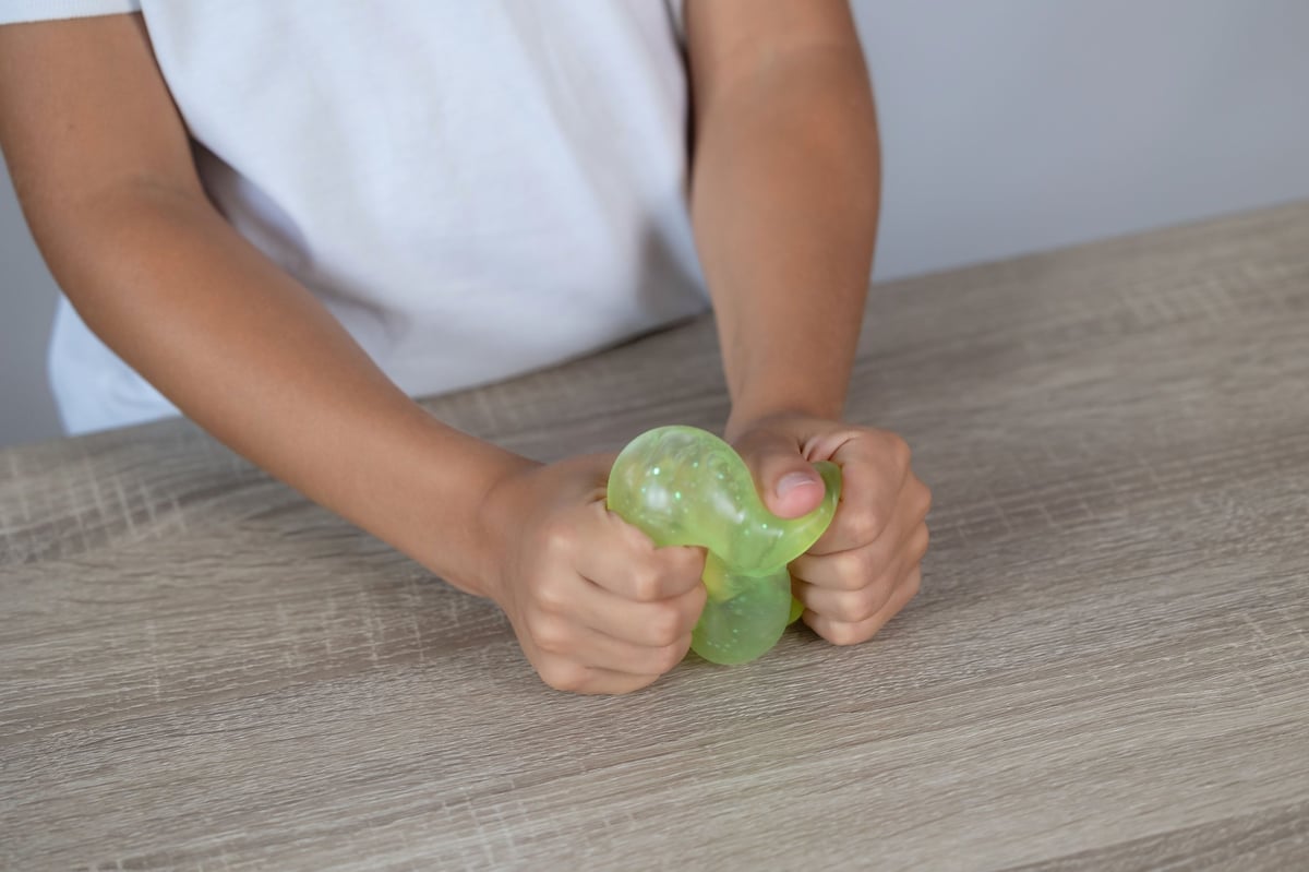 Close-up of hands squeezing a translucent green stress toy on a woodgrain table