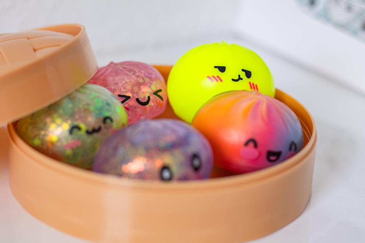 Colorful squishy dumpling toys with cheerful faces nestled in an orange steamer container